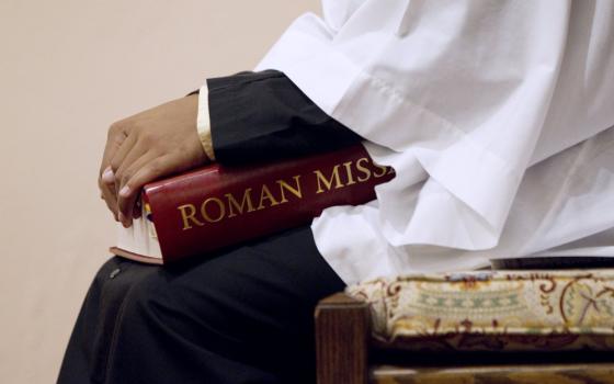An altar server holds a red book with the gold letters "Roman Mis" visible.