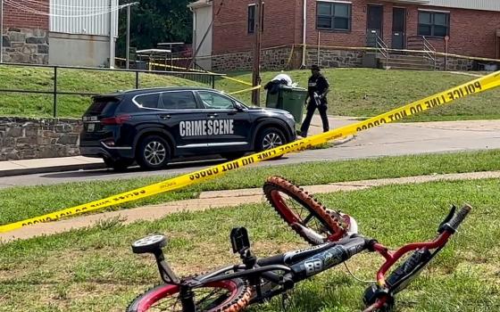 A child's bicycle, seen in a still image from video, lies on a lawn as a police officer walks down a residential street in Baltimore July 2, after a mass shooting at a Fourth of July holiday weekend block party. (OSV News/Reuters)