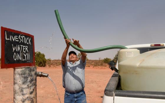 A man holds a tube in the air while standing next to a sign that reads, "Livestock water only."