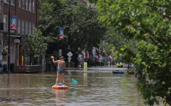 A woman rows a paddleboard down a flooded main street with American flags lining the street