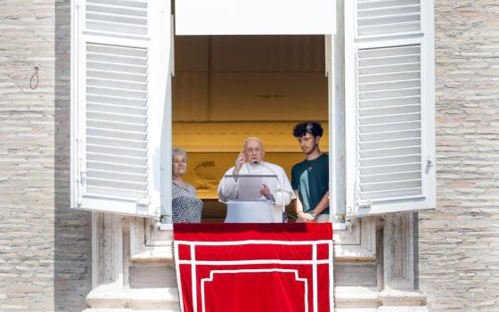 Pope Francis stands in his apartment window with an older white woman to his left and a white young man with brown hair to his right