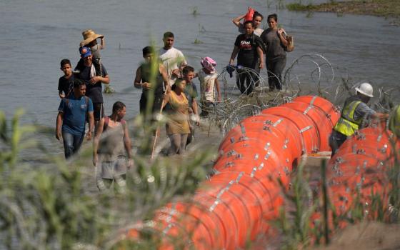 Migrants trying to enter the U.S. from Mexico approach the site where workers are assembling large buoys to be used as a border barrier along the banks of the Rio Grande near Eagle Pass , Texas, July 11. (AP/Eric Gay)