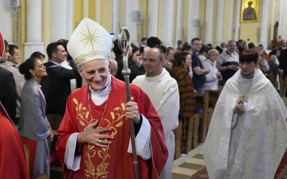 A man wearing a white and gold mitre and red vestments walks down a church aisle