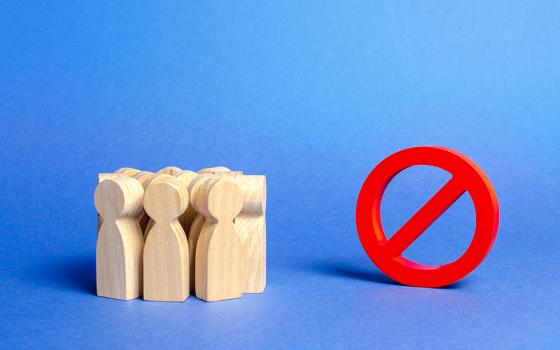 A group of wooden figures representing people stand to the side of a large red "no" symbol (Dreamstime/Andrii Yalanskyi)