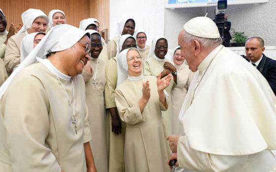 A group of sisters wearing white laugh as they stand in front of Pope Francis