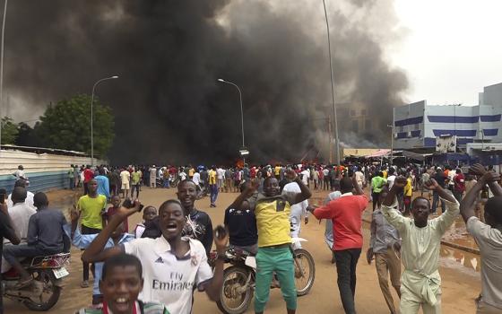 With the headquarters of the ruling party burning in the back, supporters of Niger's ruling junta demonstrate July 27 in Niamey, Niger. Defense chiefs from the West African regional bloc, ECOWAS, were to meet Aug. 17 in Ghana to discuss Niger's crisis after a deadline passed for mutinous soldiers to release and reinstate President Mohamed Bazoum or face military intervention. (AP photo/Fatahoulaye Hassane Midou, file)