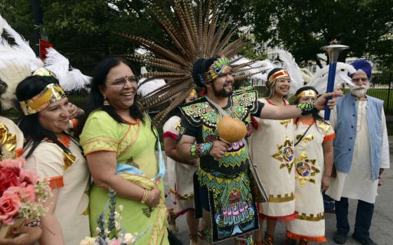 Brown people wearing feather headdresses stand next to a brown woman wearing a bindi and a brown man wearing a turban