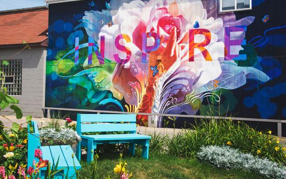 Two blue benches in a garden with a colorful mural that says "Inspire" behind them (Unsplash/Gary Meulemans)