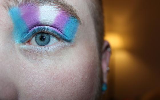 A blue eye with eye shadow in the colors of the trans flag (Unsplash/Kyle)