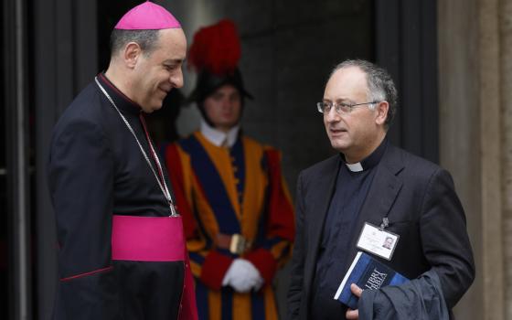 A man wearing bishop's clothes talks to a man wearing a clerical collar. A Swiss guard is visible in the background.
