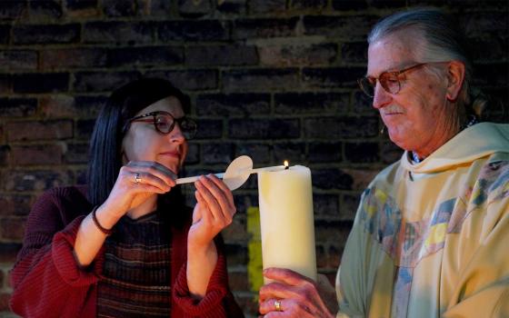 Pastoral minister Martha Ligas lights the paschal candle with "new fire" during the 2023 Easter Vigil at the Community of St. Peter in Cleveland. Pastor and administrator Bob Kloos holds the candle. (Peggy Turbett)