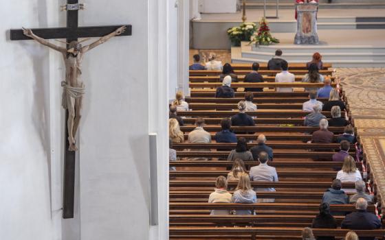 The photo focuses on a crucifix on the wall. People sitting in church pews are also visible