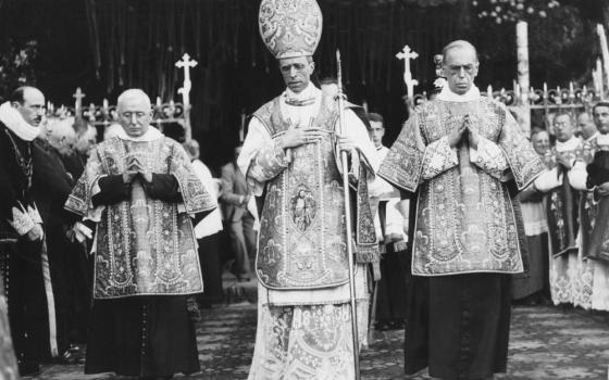 A black and white photo with a man in the middle wearing a mitre and carrying a crozier surrounded by other men in vestments