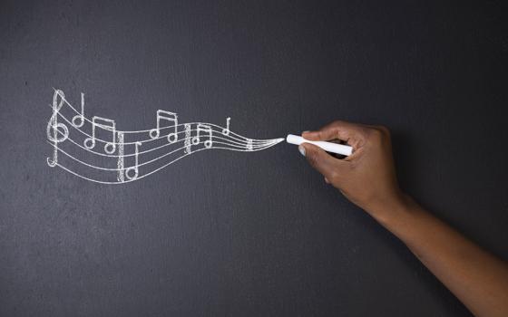 The hand of a Black person writes a bar of music in chalk on a blackboard (Dreamstime/Africa Rising Agency)