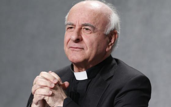 An older white man with white hair wearing a clerical collar folds his hands before his chest