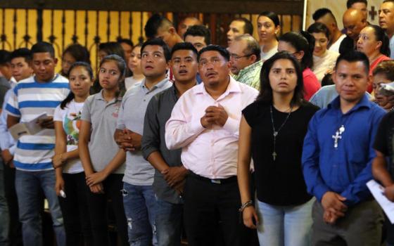 A group of brown people, many wearing crosses, assume prayerful postures