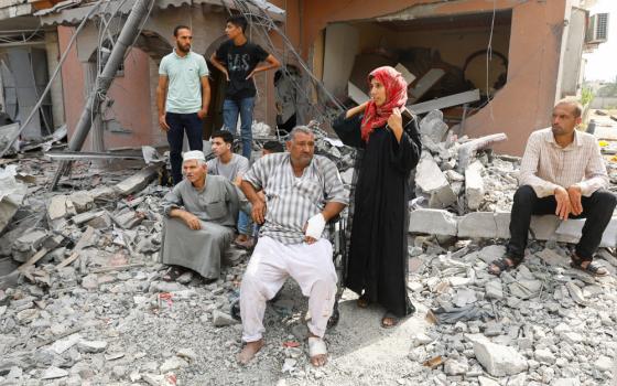 Men and a hijabi woman sit and stand around the rubble of a destroyed building