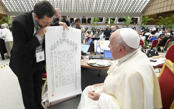A brown-haired man looks down at the print that he is presenting to Pope Francis