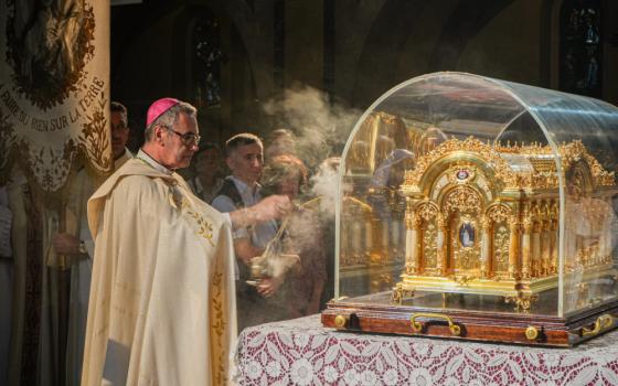A man wearing a pink zucchetto and white vestments swings incense at an ornate golden container