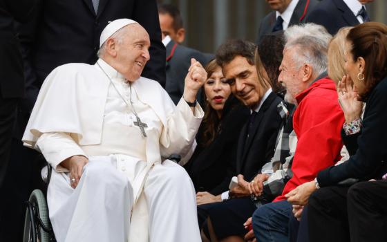 Pope Francis sits in his wheelchair and leans toward and smiles at crowd members as he is wheeled by them