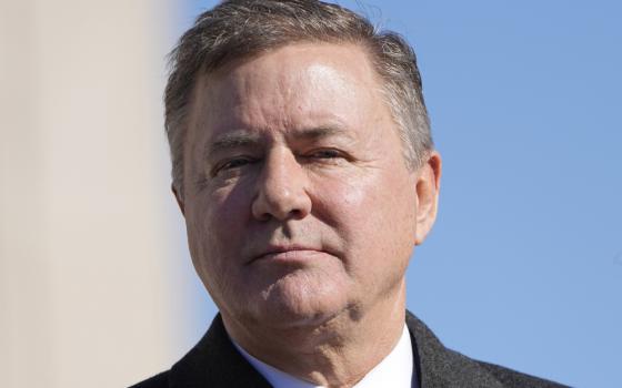 A white man with brown and gray hair wearing a suit is seen from the shoulders up