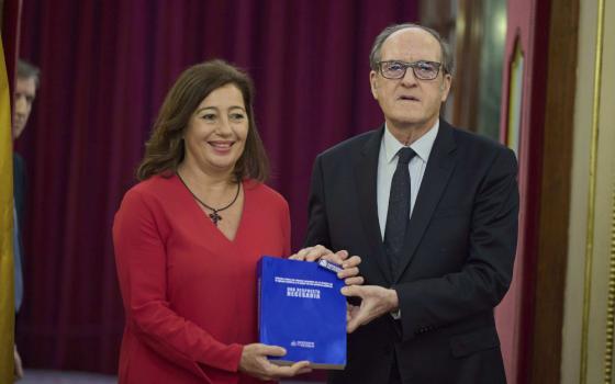 A woman and a man in Western business attire stand next to each other holding a blue book