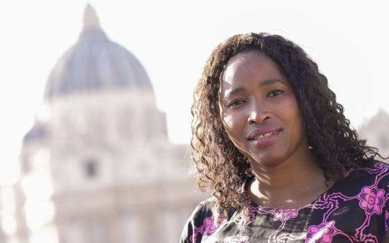 A lighter-skinned Black woman wearing a purple dress looks at the camera with St. Peter's Basilica dome visible in the background