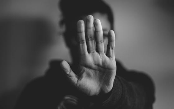 A hand put up in front of a person's face in a gesture of "stop, stay away" (Unsplash/Nadine Shaabana)