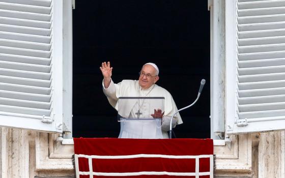 Pope Francis smiles and waves from his apartment window with his other hand on the clear lectern