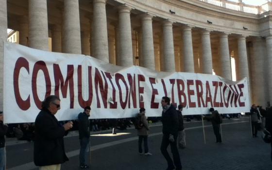 People hold a banner that reads "Comunione e Liberazione" standing before the pillars in St. Peter's Square