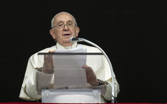 Pope Francis holds a sheet of paper and speaks into a microphone