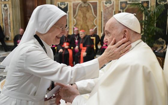 A woman religious wearing a white habit puts a hand on Pope Francis' cheek