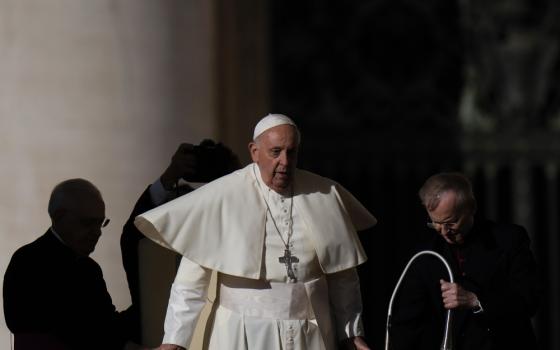 Pope Francis walks with his mozzetta flying out as other men surround him in the shadows