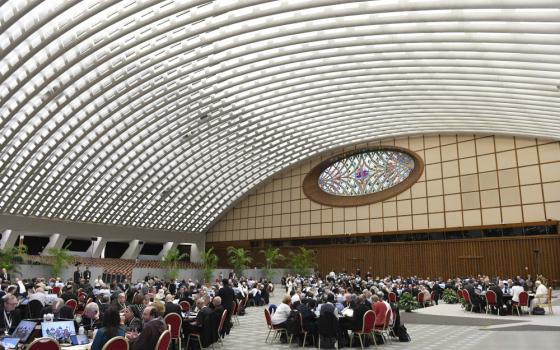 People gather around round tables spread across a large audience hall with an arched roof