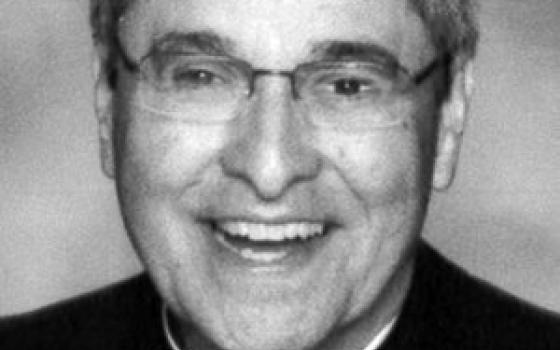 A black and white photo of an older priest wearing glasses and smiling broadly