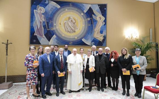 Pope Francis and a group of people pose for a photo below an abstract tapestry