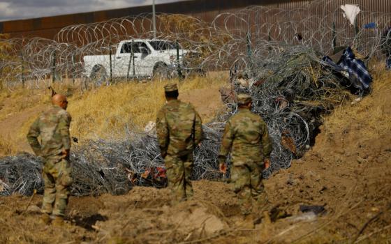 People in camo uniforms stand next to twisted razor wire. Clothing is caught in different parts of the razor wire.