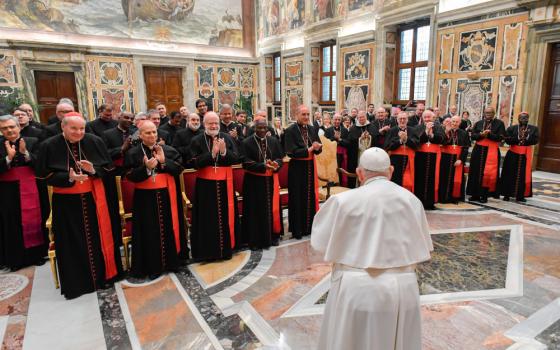 Pope Francis faces and stands in front of a group of men wearing cardinals' cassocks