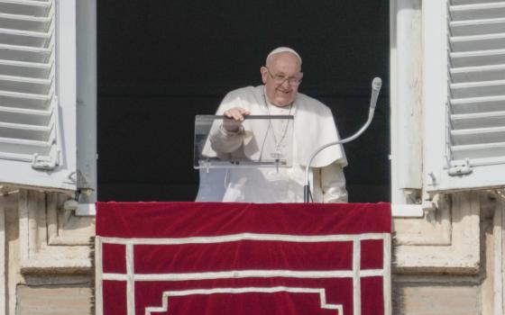 Pope Francis smiles and peers over the edge of his apartment window with one hand on his clear lectern 
