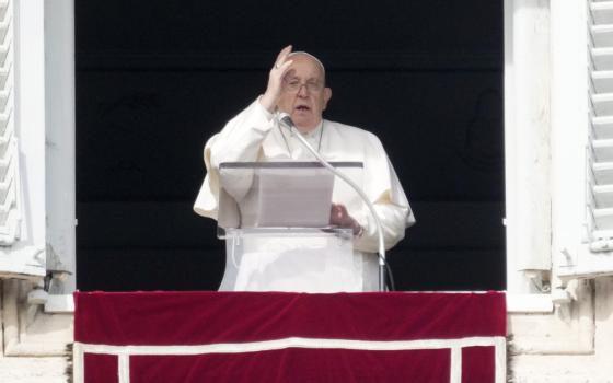 Pope Francis raises his right hand to make the sign of the cross from his apartment window