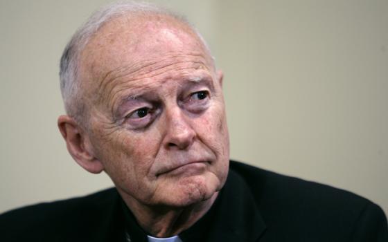 An older white man wearing a clerical collar looks off the camera with a serious expression