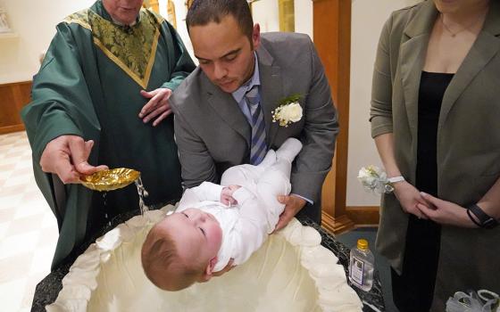 Julio Prendergast holds his 5-month-old son, Gabriel James, as he is baptized by Msgr. Frank Schneider Nov. 12, 2022, at St. John the Baptist Church in Wading River, New York. Looking on is the baby's mother, Christina Prendergast. (OSV News/Gregory A. Shemitz)