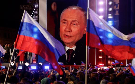 Vladimir Putin cast on screen during rally, framed by Russian flags