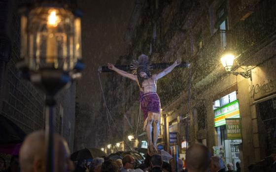 Large life-size crucifix depicting Holy Christ of the Blood carried at night through rain. 