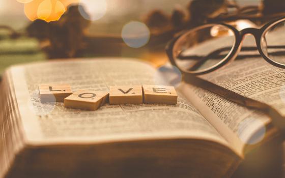 Letter tiles spell out the word "love" on top of a Bible laying open, with a pair of glasses next to the letters.(Unsplash/Emmanuel Phaeton)