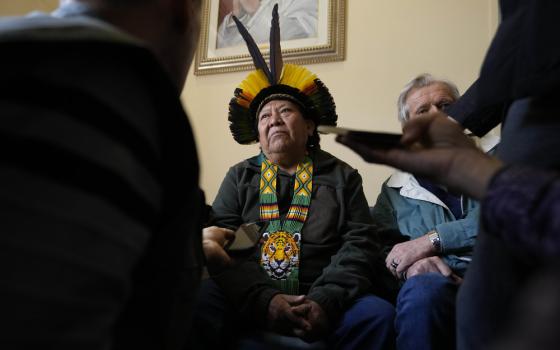 Man wearing traditional Amazonian garb sits while fielding questions