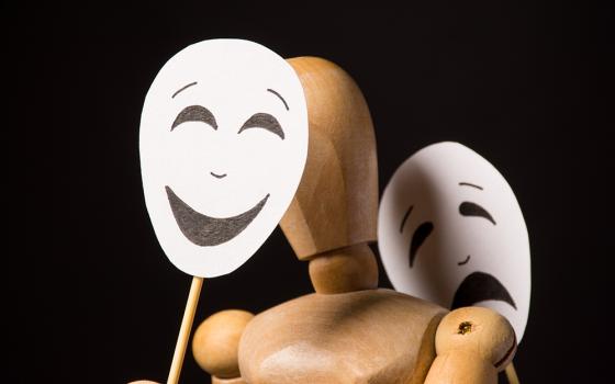 Wooden human figure holds a happy mask and a sad mask (Dreamstime/Oksana Volina)