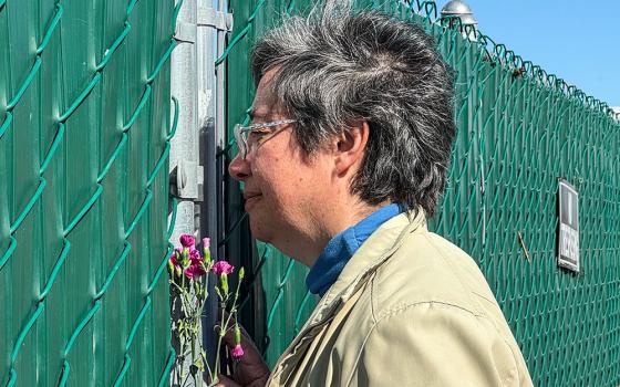 Sr. Clara Malo Castrillón, provincial of Mexico's Society of the Sacred Heart, looks through an opening in a fence where you can see tombs fenced off from the rest of Terrace Park Cemetery in Holtville, California, during a Feb. 7 stop. Sisters stopped to pray and threw flowers over the locked fence toward the bricks that serve as tombstones where remains include those of anonymous migrants. (GSR photo/Rhina Guidos) 