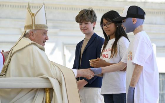 Pope Francis, vested, sits as he receives children. 
