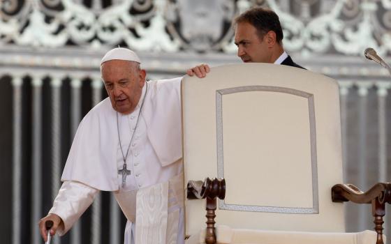 Pope Francis leans on cane as he prepares to sit. 